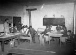 school children gather around two wooden desks in a wooden schoolhouse